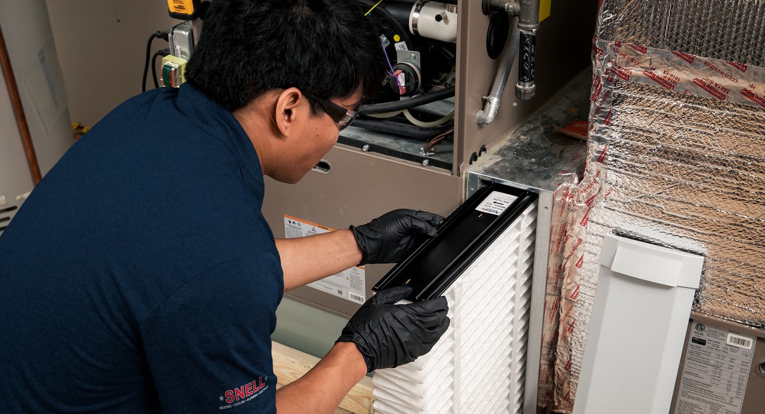 A professional Snell HVAC technician replacing a clean pleated air filter in an indoor air handler unit during a routine AC maintenance tune-up.