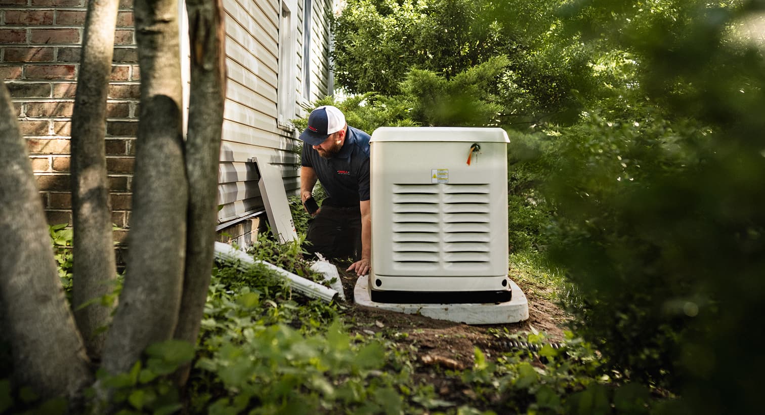 A professional Snell technician inspects a large, beige whole-home standby generator installed on a concrete pad outside a residential house.