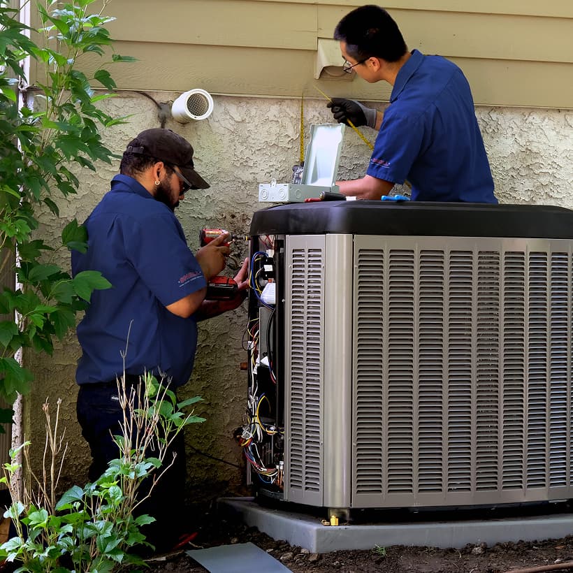 Two Snell HVAC technicians installing a brand-new residential outdoor air conditioning condenser unit during a home AC replacement service.
